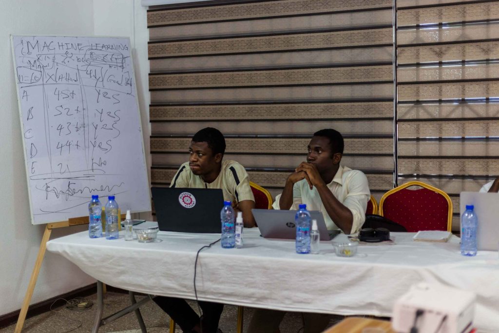 Two men sitting at a table with laptops.